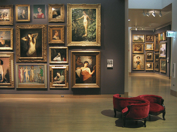 A circular chair in a large room whose walls are covered in oil paintings