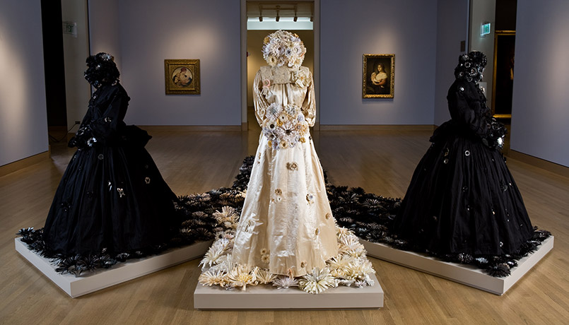 Three dress arranged on pedestals in a museum gallery