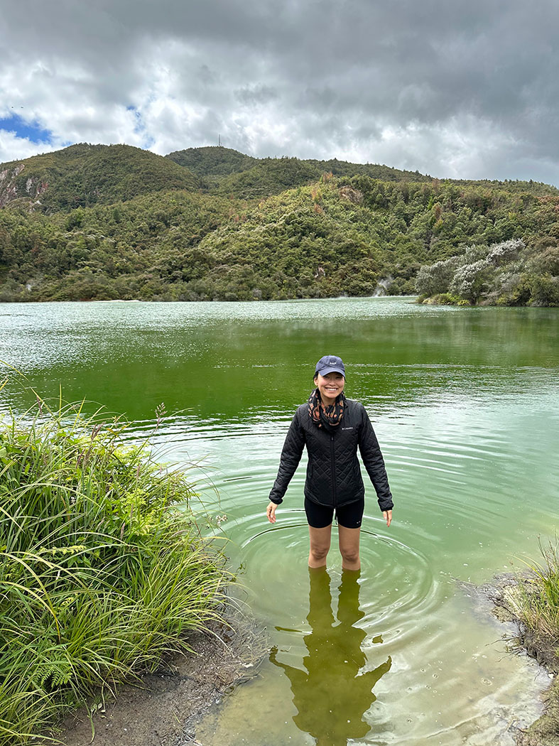 A person standing up to their knees in a large, green body of water in nature