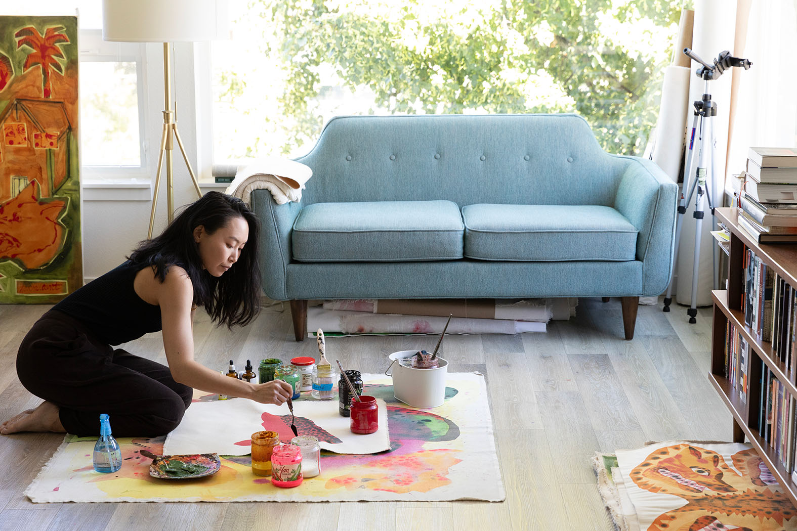 A person painting on the ground in a room with a blue couch
