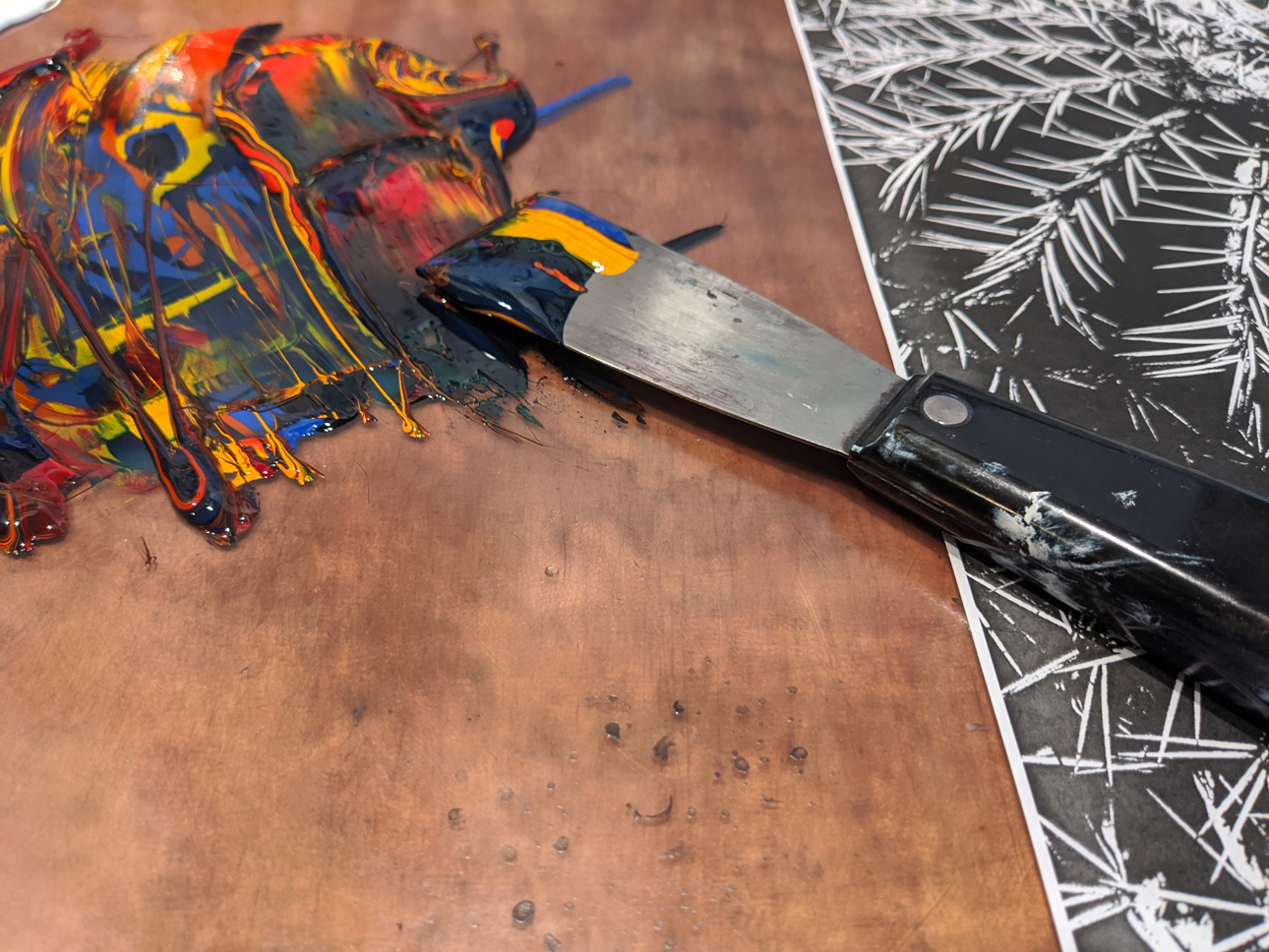 Photo of a palate knife with four colors of ink partially mixed on a tabletop surface