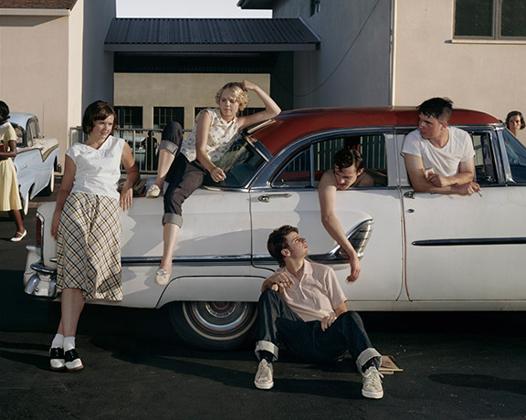 People sitting in and next to a car in a 1950s scene