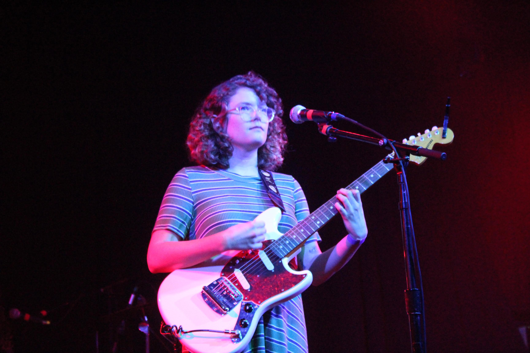 Shannon Bodrogi standing onstage behind a mic, holding a guitar