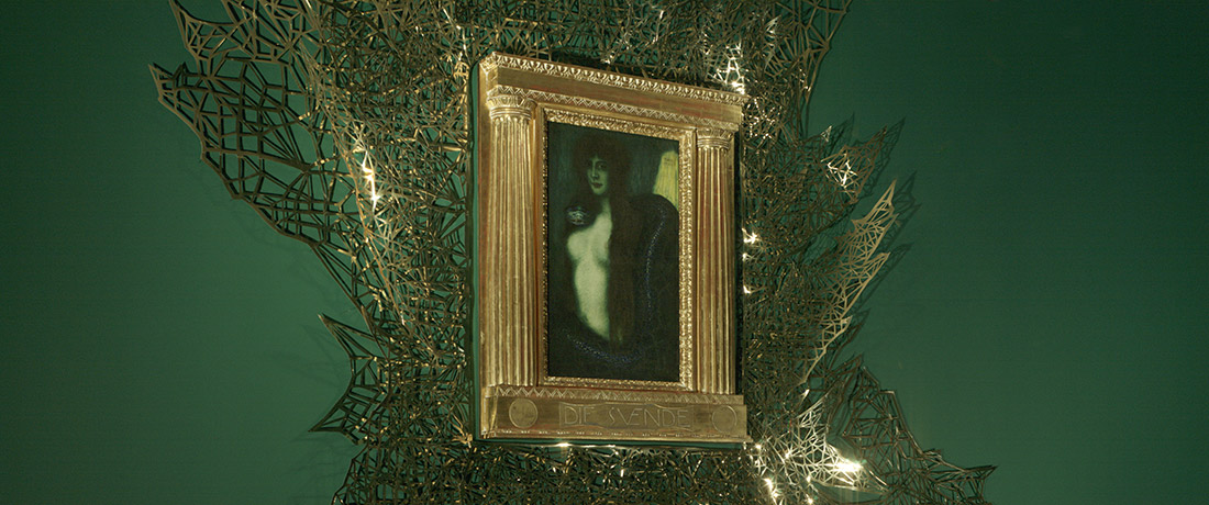 A painting of a woman and snake in an opulent gold frame surrounded by a geometrical gold pattern