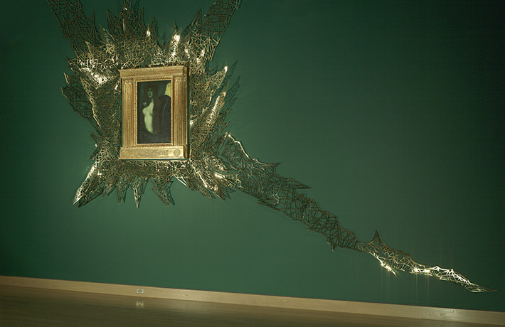 A painting of a woman and snake in an opulent gold frame surrounded by a geometrical gold pattern