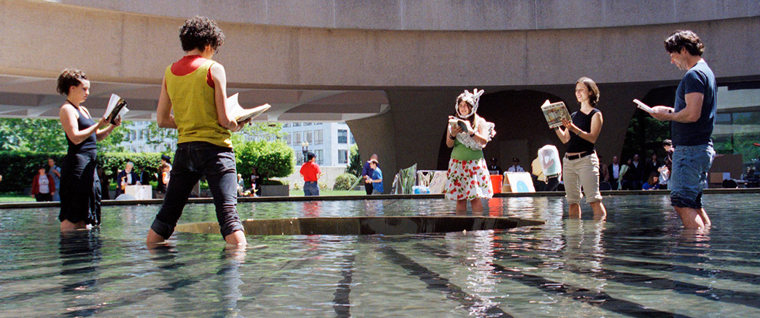 People standing in a shallow pool reading books as part of a performance
