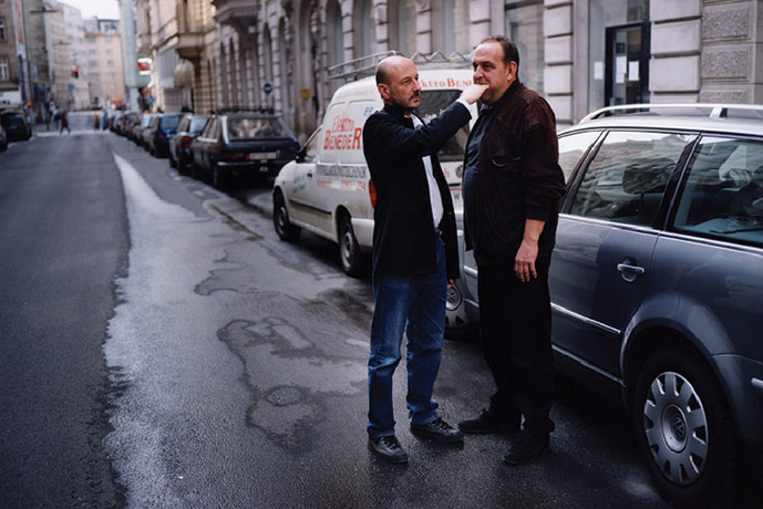 A photograph of a man reaching inside another man's mouth