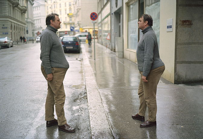 Photograph of two men identical men dressed in similar ways facing each other with their eyes closed