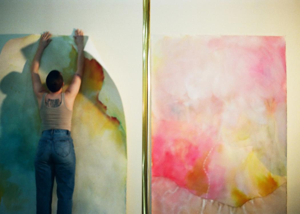 Photo of Lydia Jewel Gerard hanging an artwork on a wall next to another colorful artwork