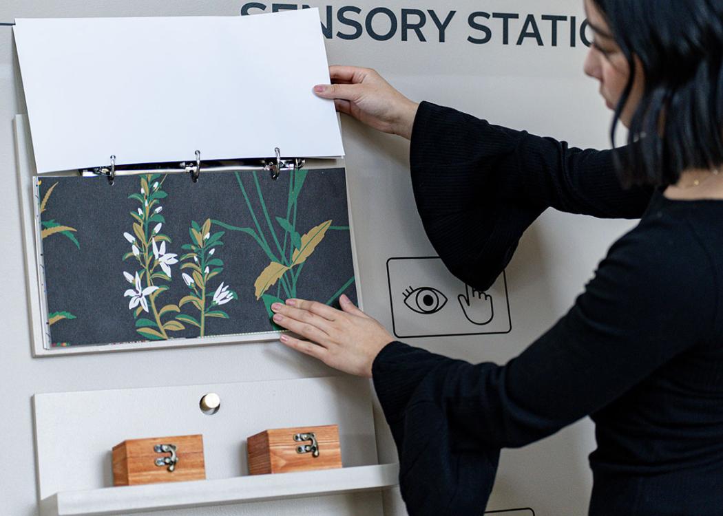 A person touching a sample of a floral wallpaper mounted vertically on a cart