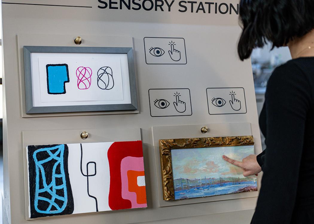 A person touching a sample of a framed oil painting on a mobile cart