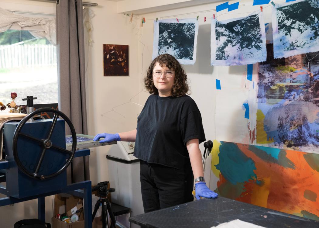 Photo of Shannon Bodrogi in their studio with their art behind them