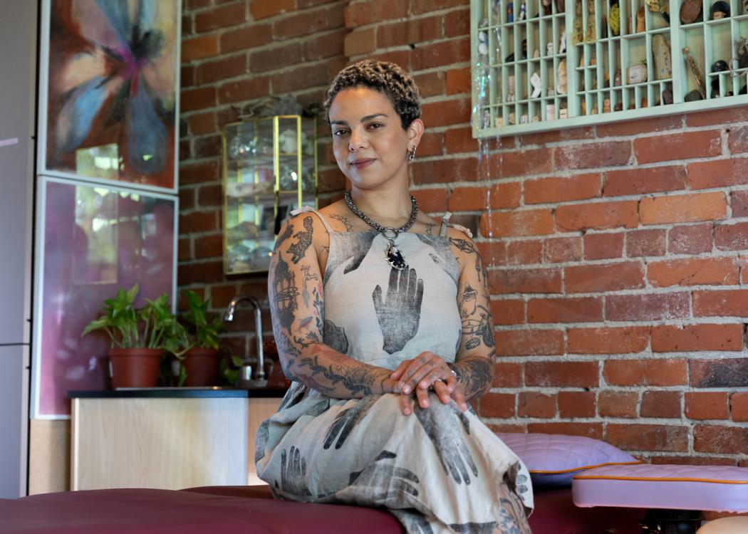 Emma Kates-Shaw sitting on a tattoo table at their studio looking directly at the camera