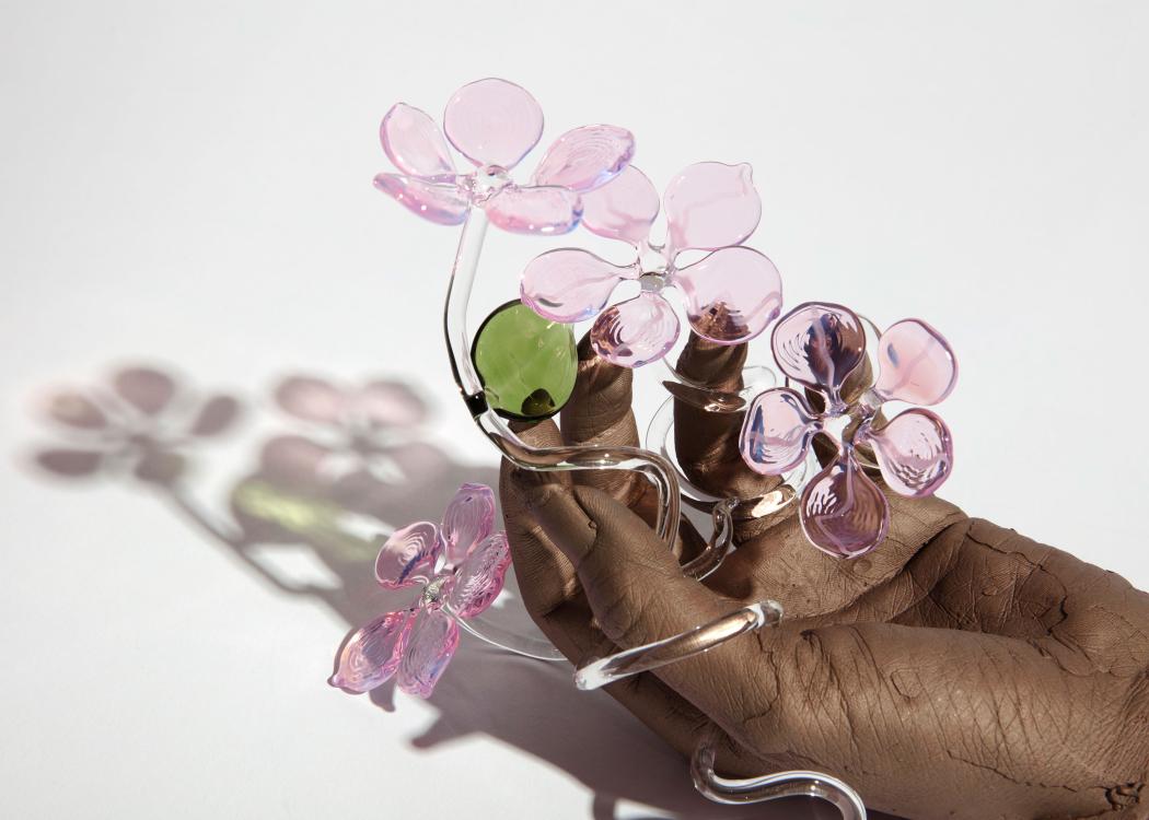 Kelly Akashi sculpture, bronze hand holding light pink glass flowers with green leaves