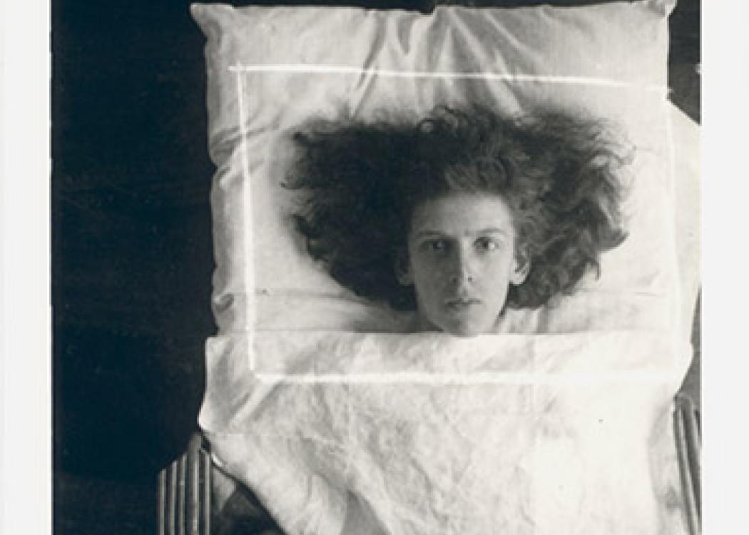 A black and white photo of a person on a bed with their hair splayed out around their head on a pillow