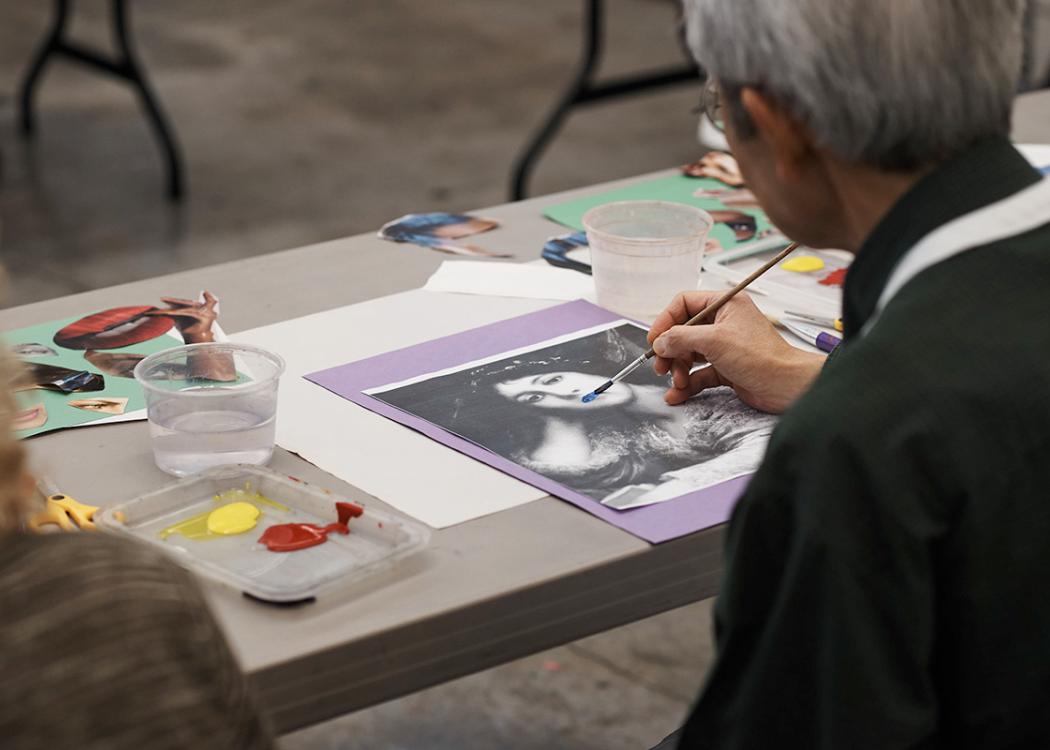 An older adult working on artwork that involves painting over a printed image