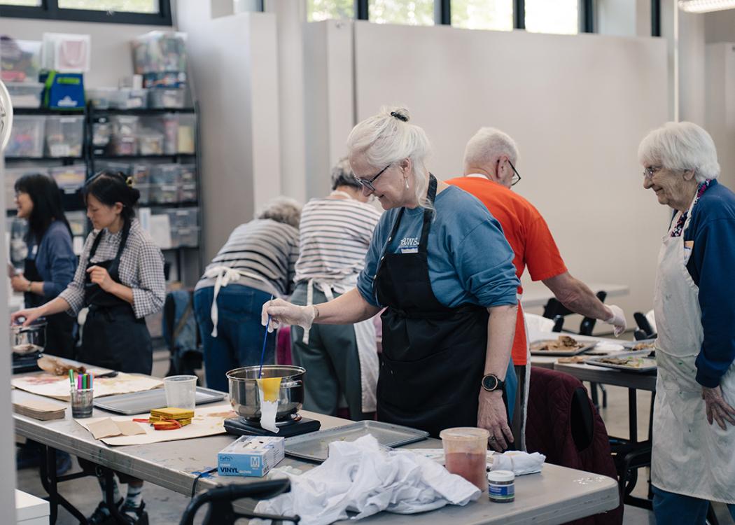 An older woman working on an art activity dipping a fabric into a bowl of dye