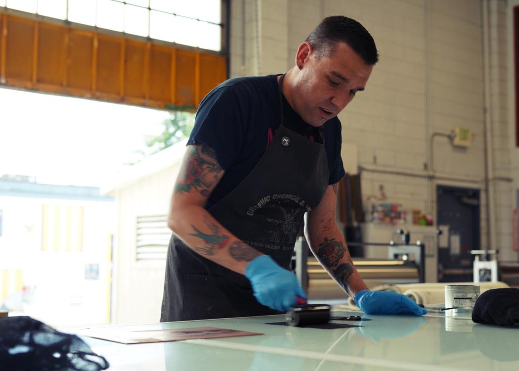 Photo of Ben Moreau, a man with short dark brown hair, rolling ink out in a print shop