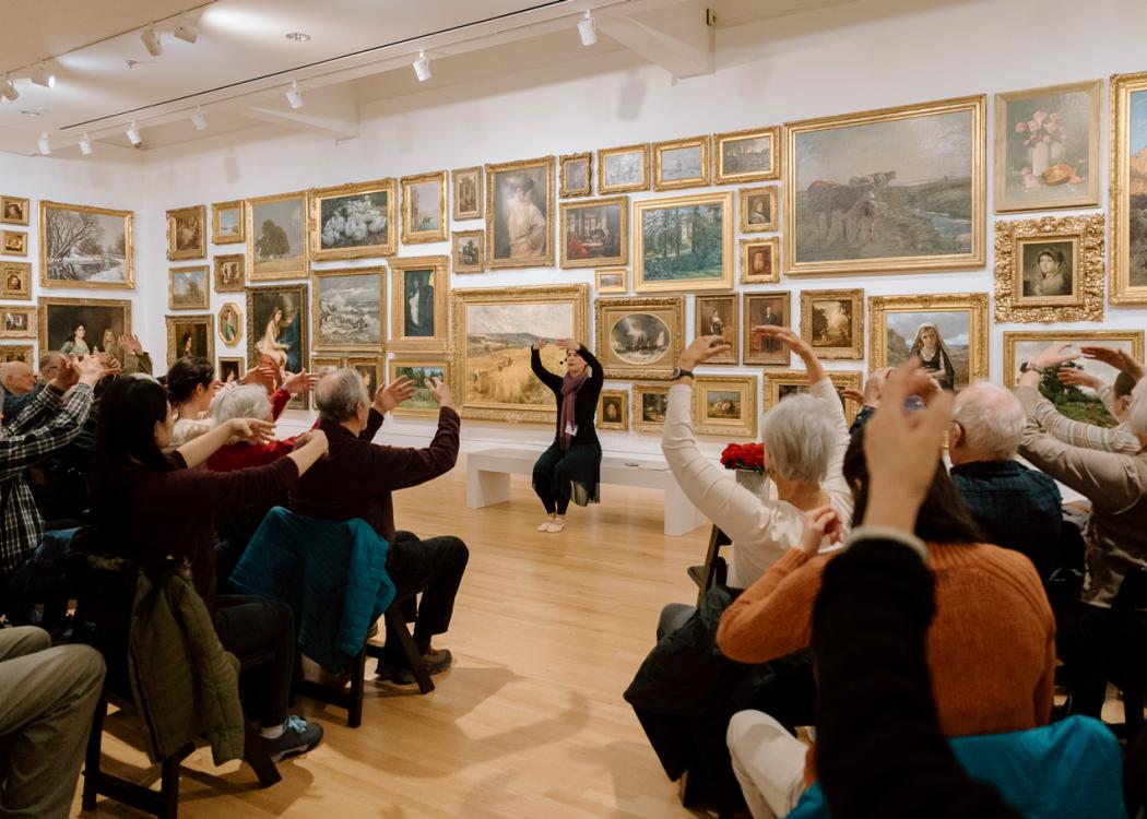 Dr. Julia Becke leading seated movement with a large group of Creative Aging participants in the Salon