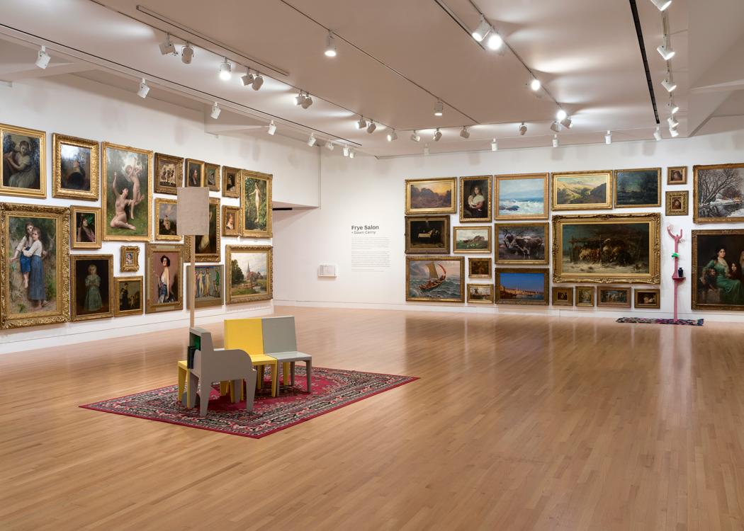 A large room with art covering the walls. Colorful chairs are grouped in the middle of the room.