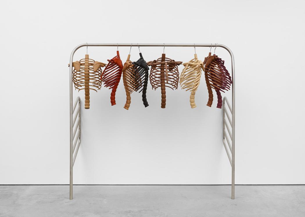 An assortment of ribcages and spines made of different colors of wood hanging from a thick metal rack