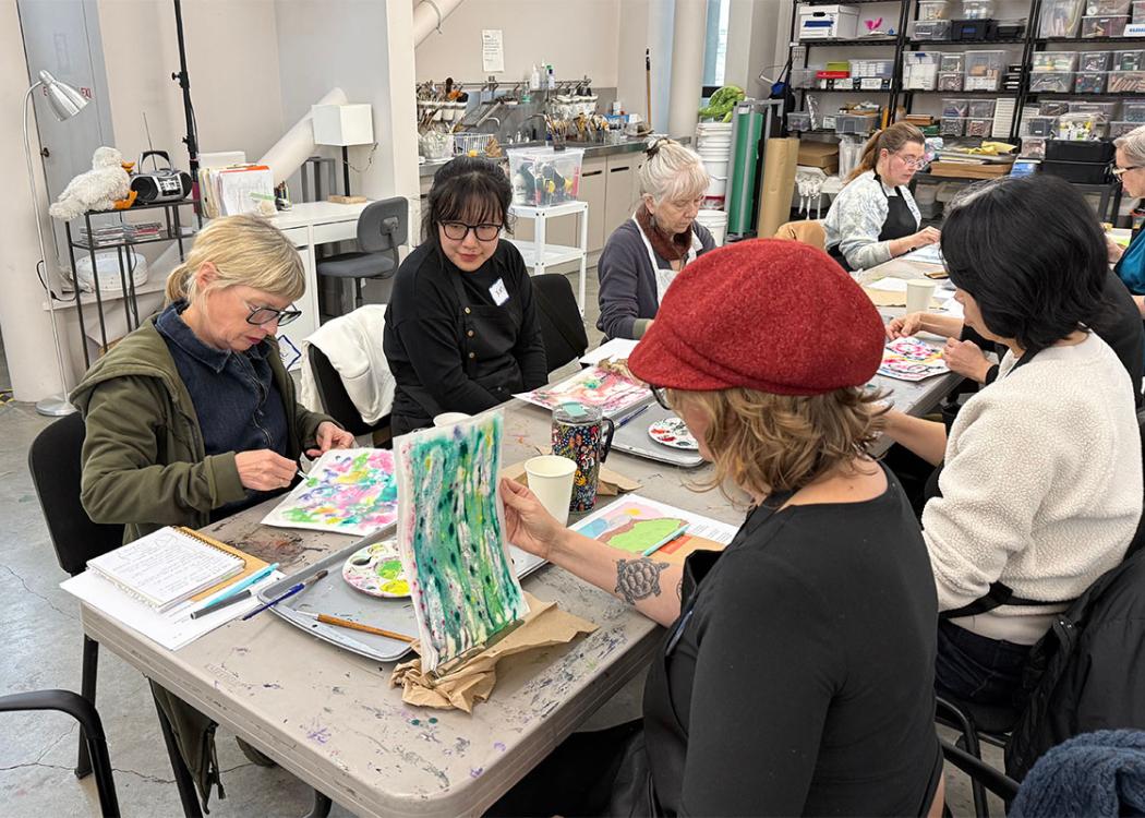 People sitting at a long table in an art studio space working on colorful paintings