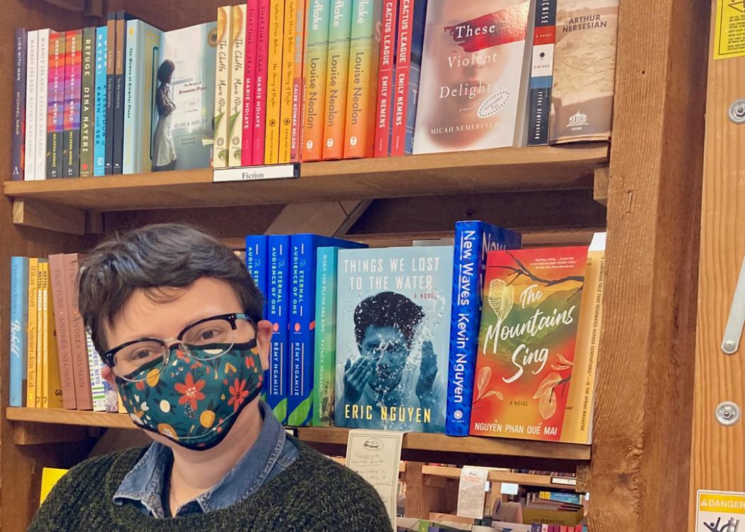 Photo of Micah Nemerever in front of a bookshelf holding his novel "These Violent Delights"