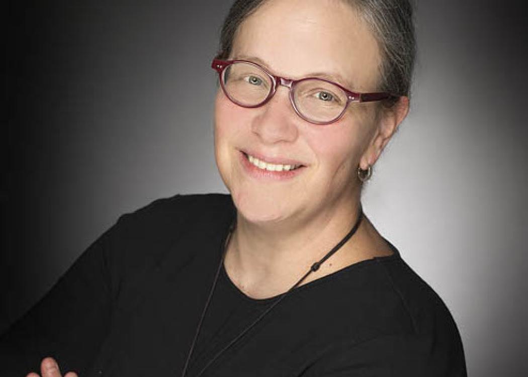 Color photograph of a white woman wearing glasses, smiling, with arms crossed