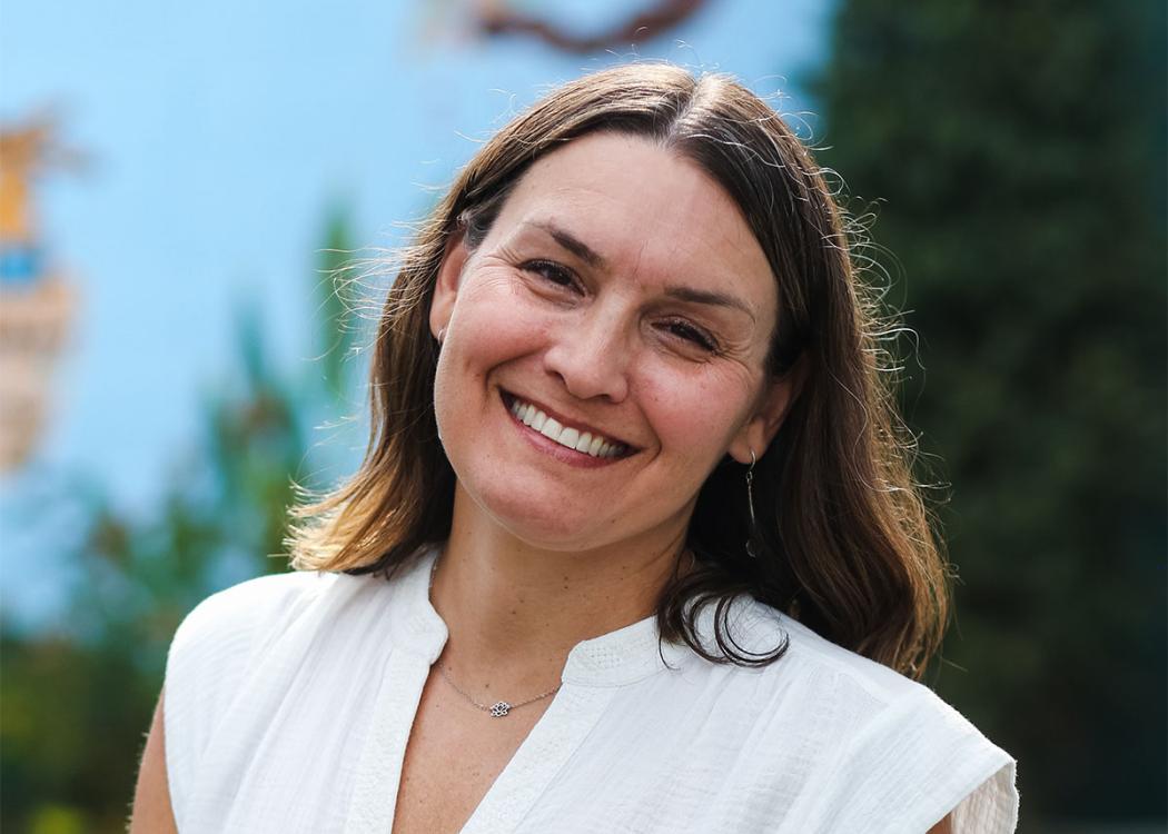 Crop of a professional headshot style photograph of a smiling woman wearing a white top