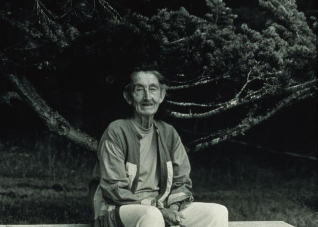 A black and white photograph of an older woman sitting on an outdoor bench