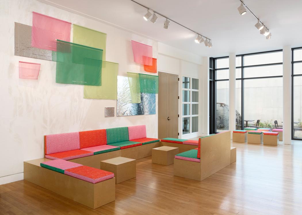 A large interior space, well lit through a glass wall, with low benches and fabric and reflective panels on the walls