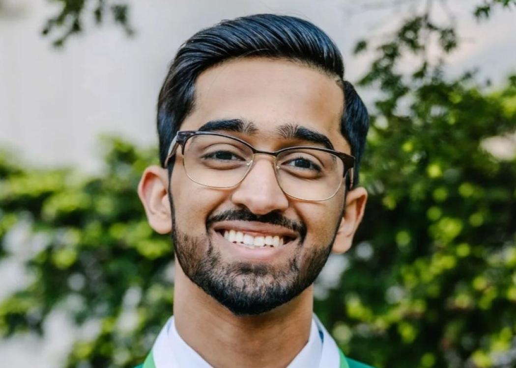 A professional headshot style photograph of a smiling younger man