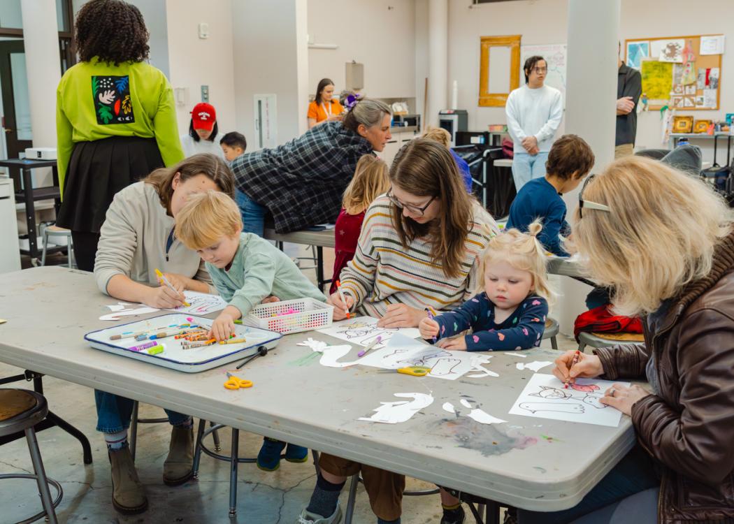A group of children and adults work on an art project in a well-lit studio space