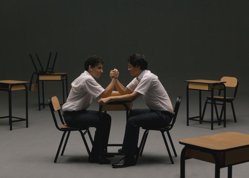Video still of two boys arm wrestling while sitting in school desks
