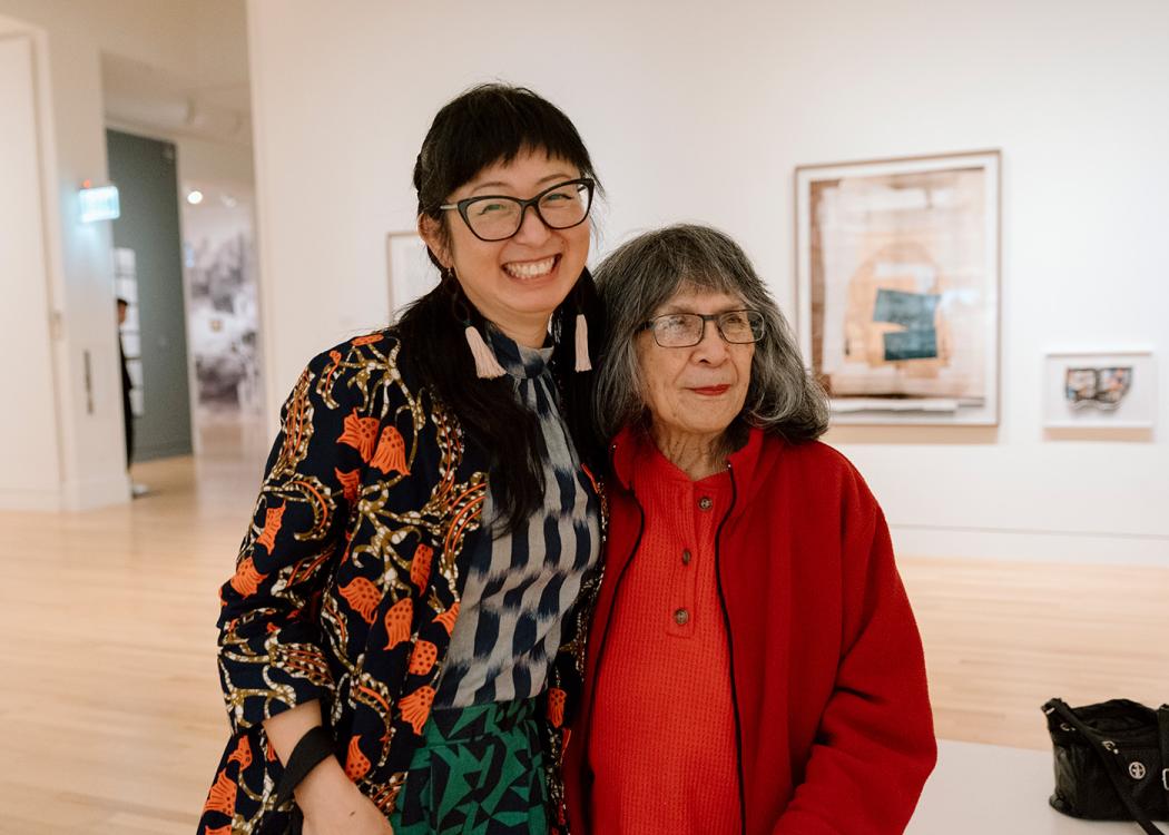 Two Asian women, one older, standing next to each other and smiling in a large open art gallery space