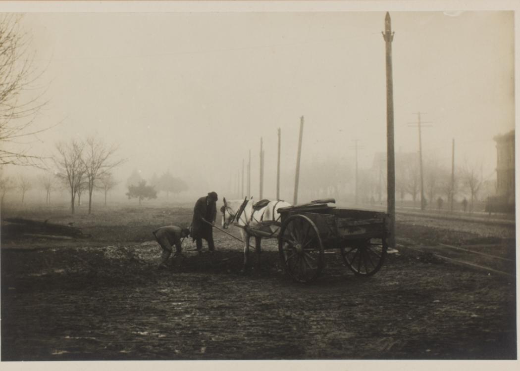 A sepia-toned photograph of two people with a horse pulling a small, open carriage