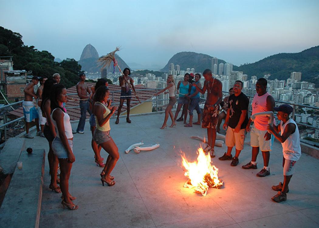 Still from a video of people dancing around a small fire on the roof of a building