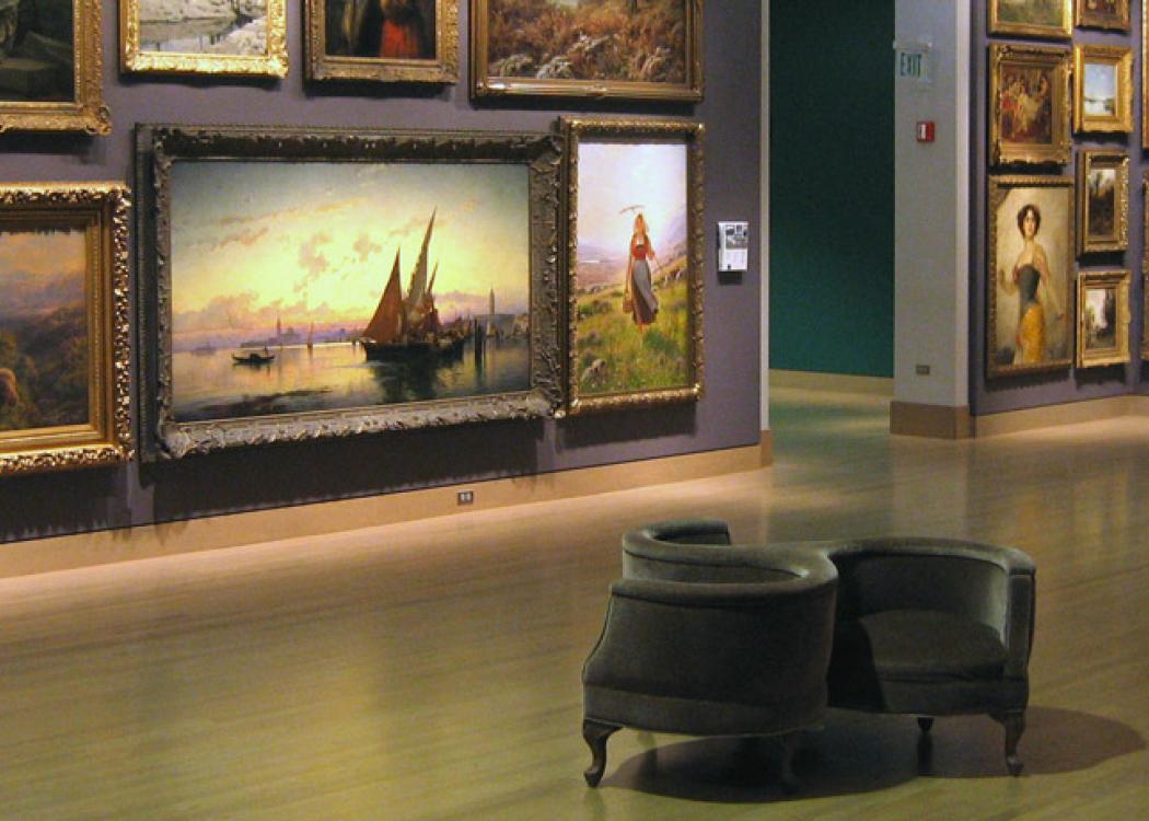 A circular chair in a large room whose walls are covered in oil paintings