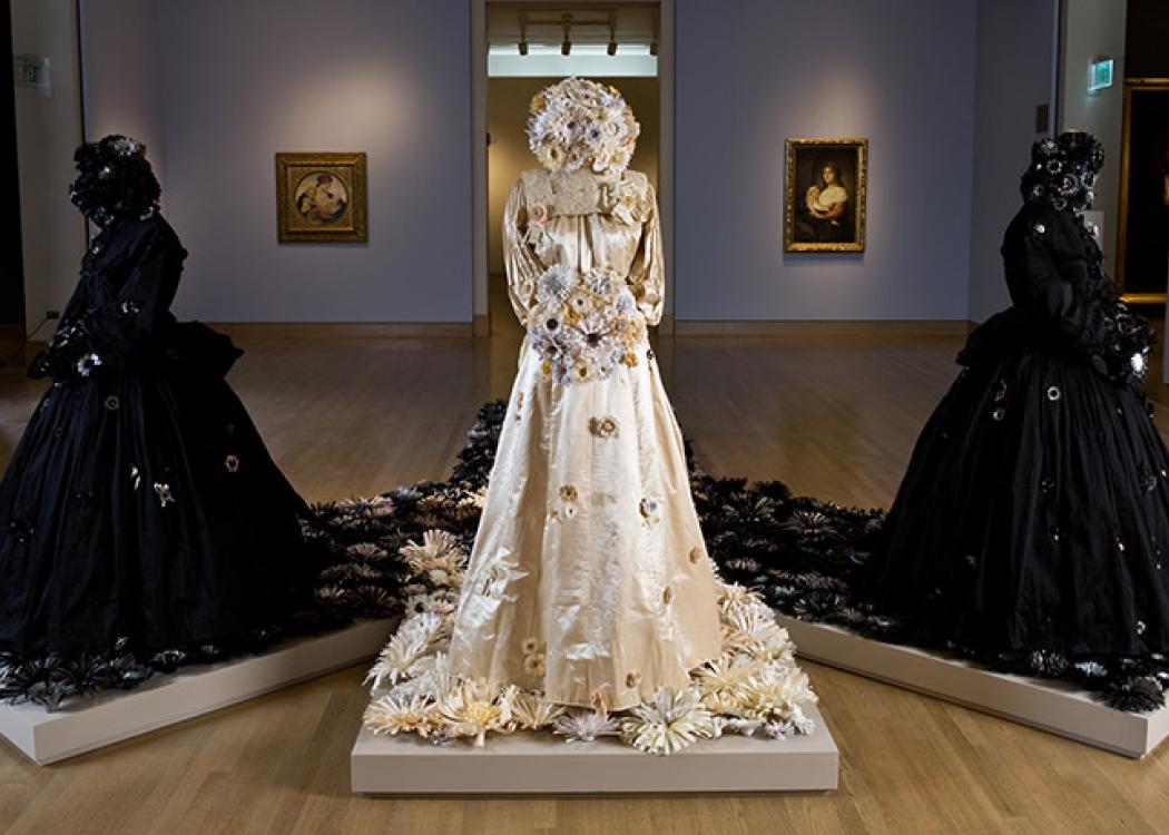 Three dress arranged on pedestals in a museum gallery