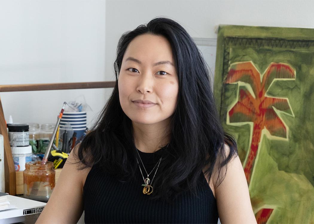 An Asian woman wearing a black top sitting in front of a large artwork