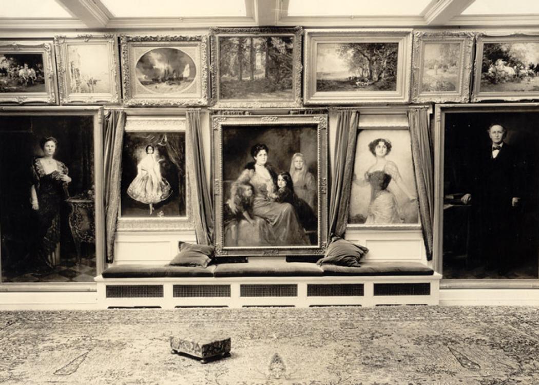 A sepia photo of the interior wall of a home covered in paintings