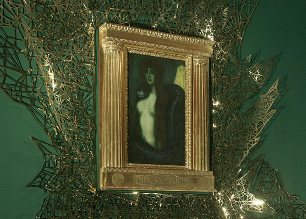 A painting of a woman and snake in an opulent gold frame surrounded by geometric gold patterns