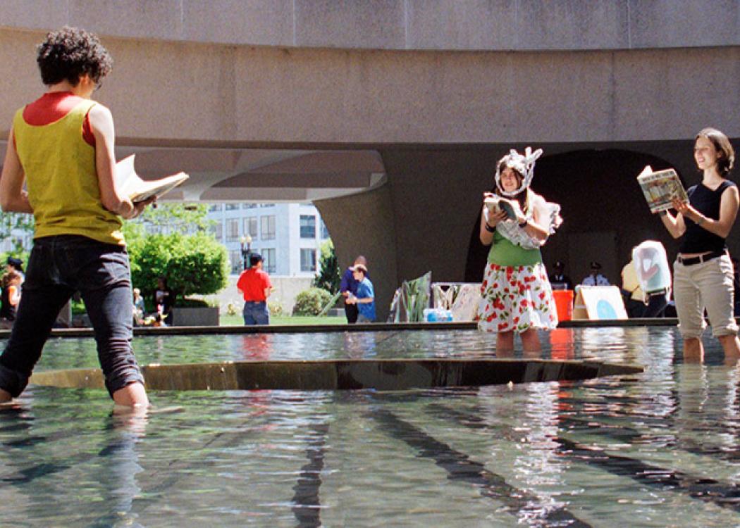 People standing in a shallow pool and reading from books as part of a performance