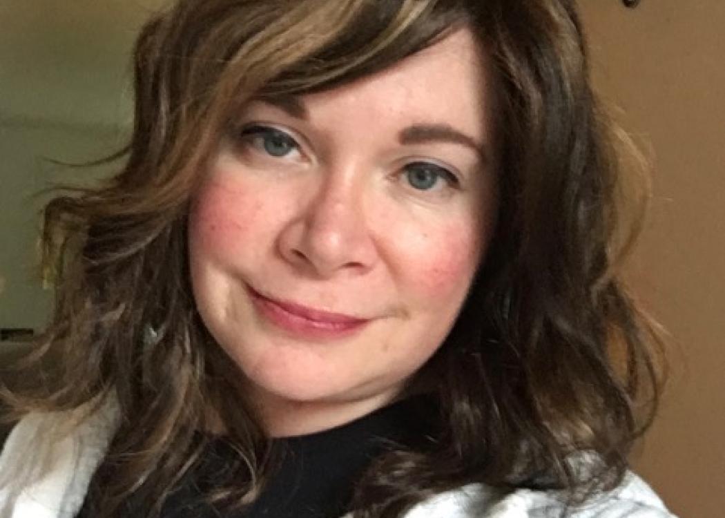 Photo of Jennifer Kulik, a woman with long brown hair wearing a black shirt and white sweater