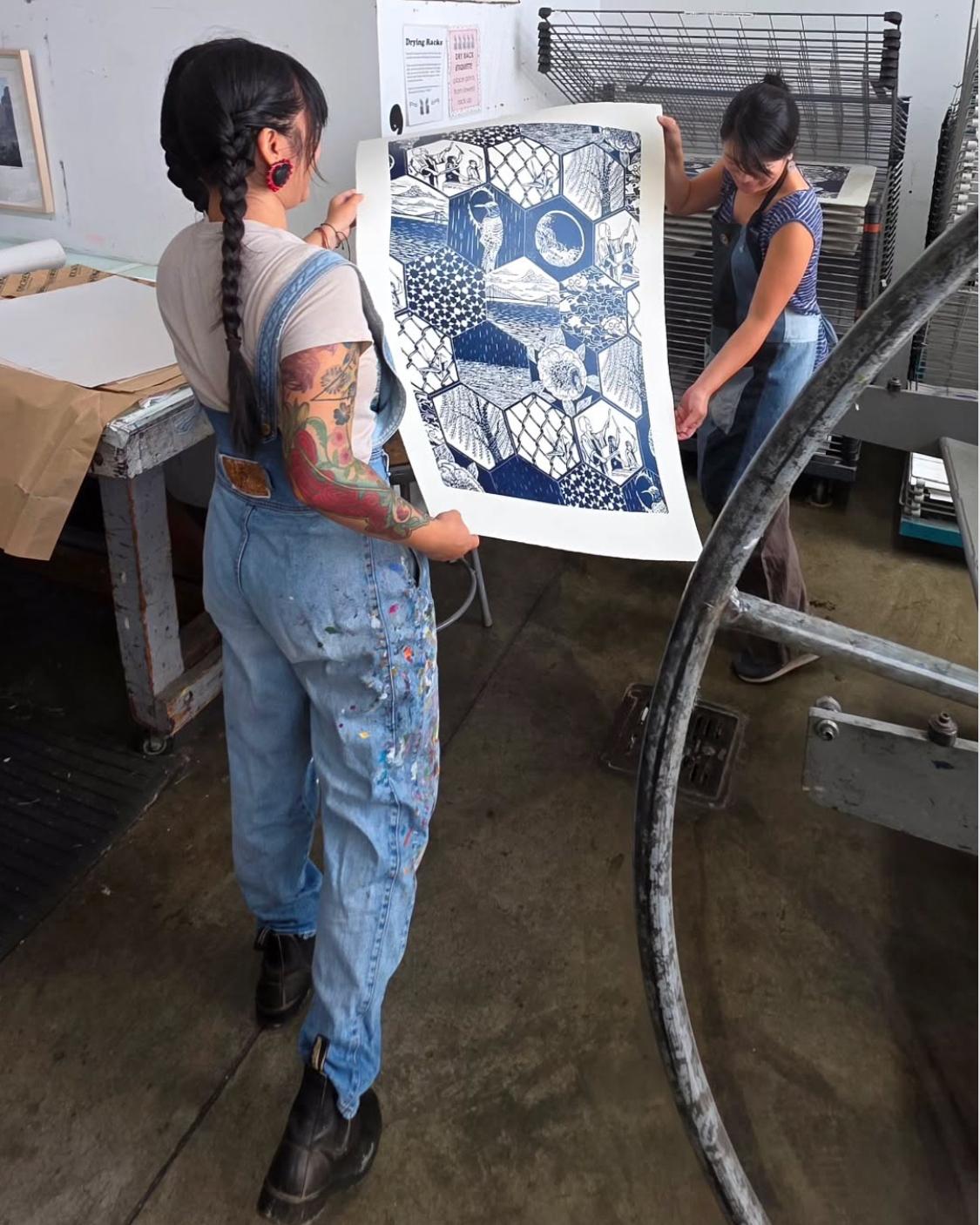 Artists Saiyare Refaei and Yoshi Nakagawa holding a print of "Sound", which is blue and white, in an art studio