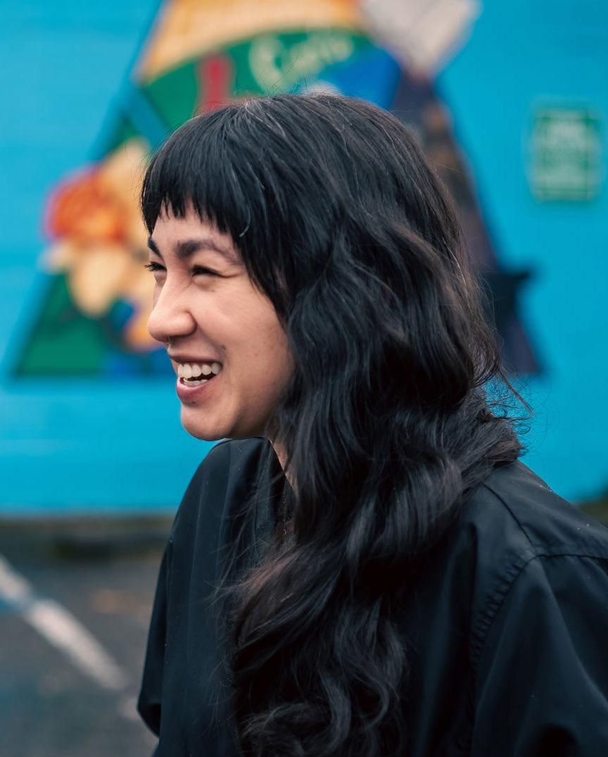 Saiyare Refaei, a person with long black hair worn down, smiling and looking out of frame