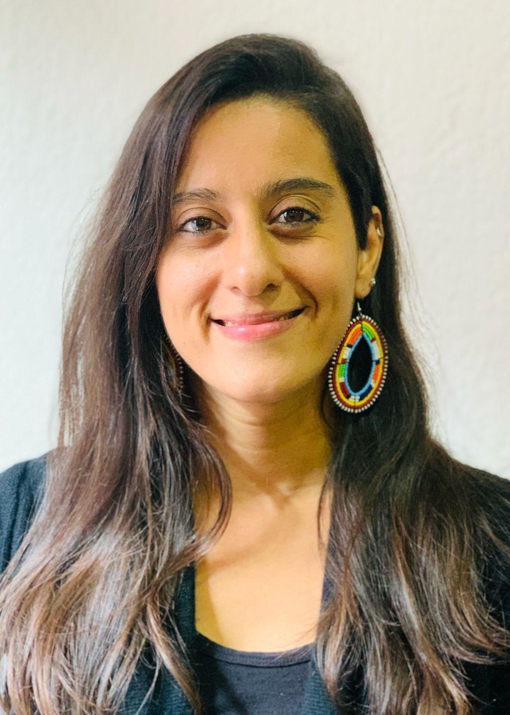 A professional headshot style photograph of a woman with a large, beaded earring