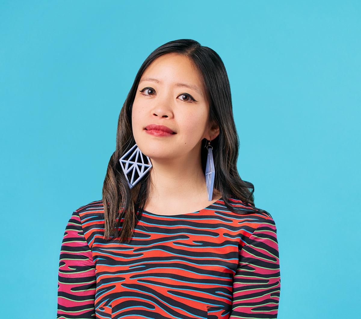 A professional headshot photo of a younger Asian woman against a solid blue background