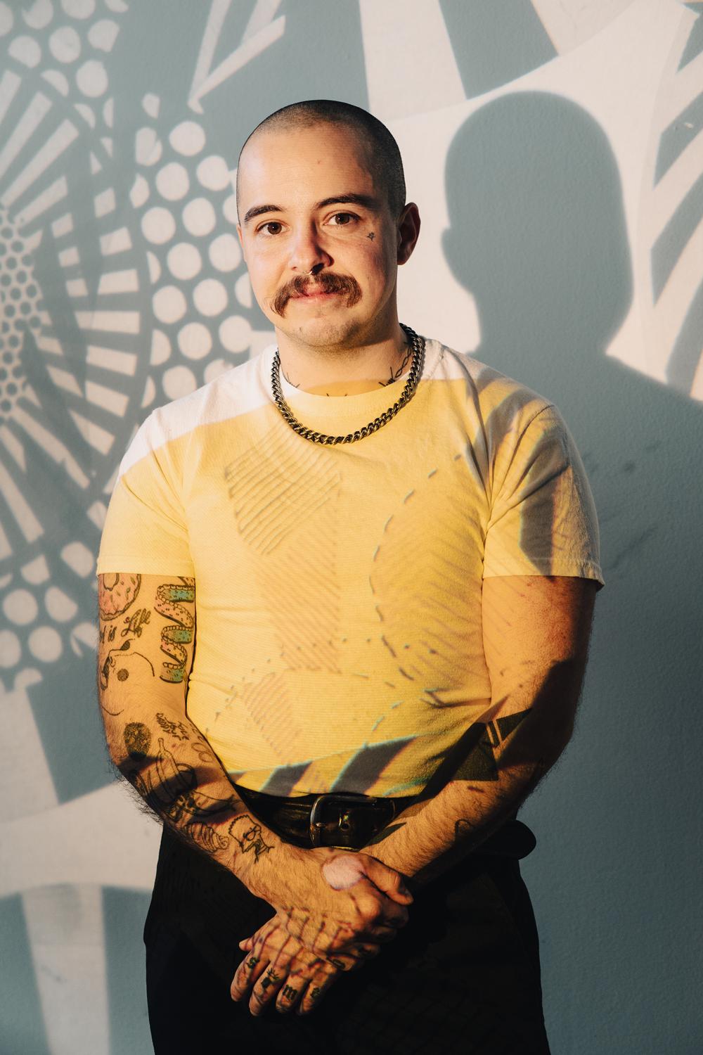 Photo of Lane Bestold standing in a white shirt and black pants in front of a patterned wall