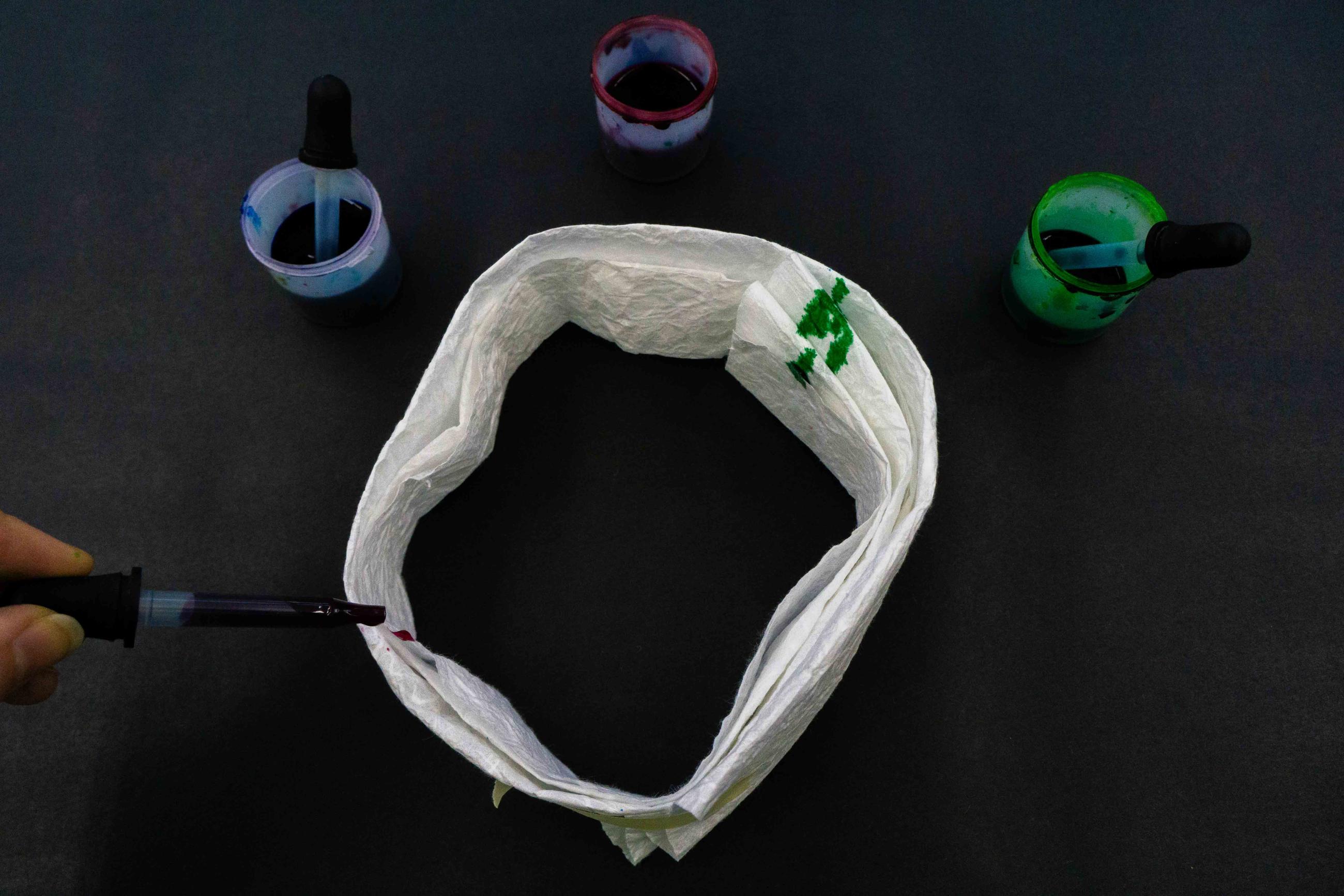 Photo of someone dripping paint from a dropper onto a ring of folded paper